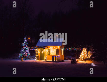 Cute, wooden painted yellow private children`s play house in home garden, decorated with Christmas LED string lights outdoors in cold snowy winder nig Stock Photo